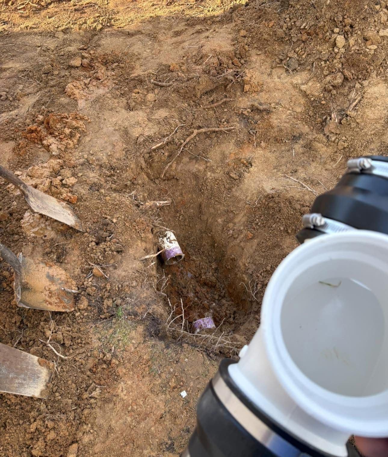 Excavated area showing buried can and tools for plumbing or repair work.