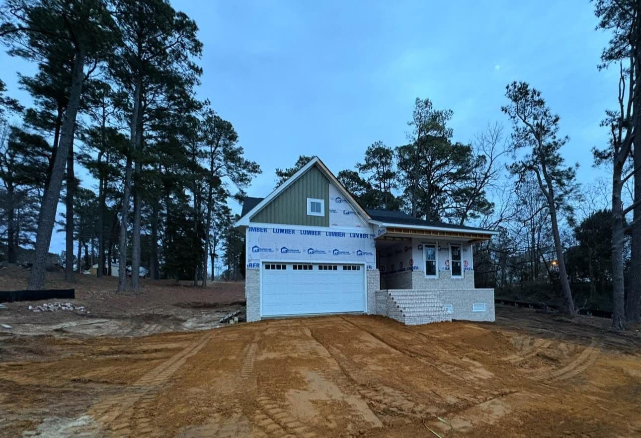 Newly built home with a gray and white exterior, surrounded by trees and construction site.
