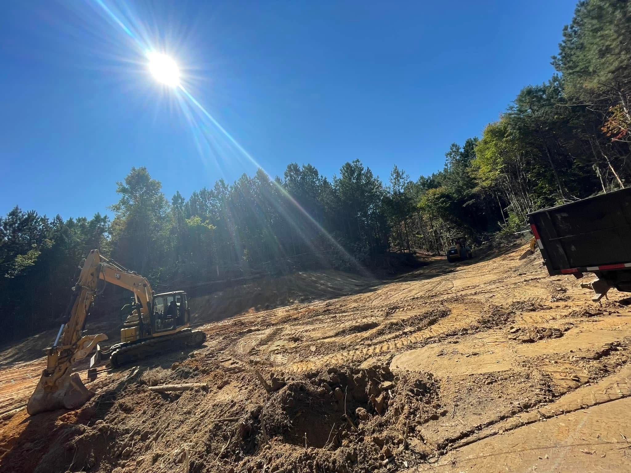 Excavator working on a construction site under a bright sun with forested background.