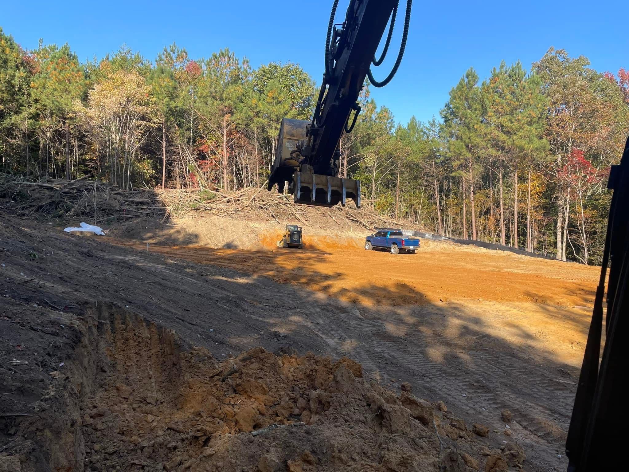 Excavator and machinery working on a cleared construction site with trees in the background.