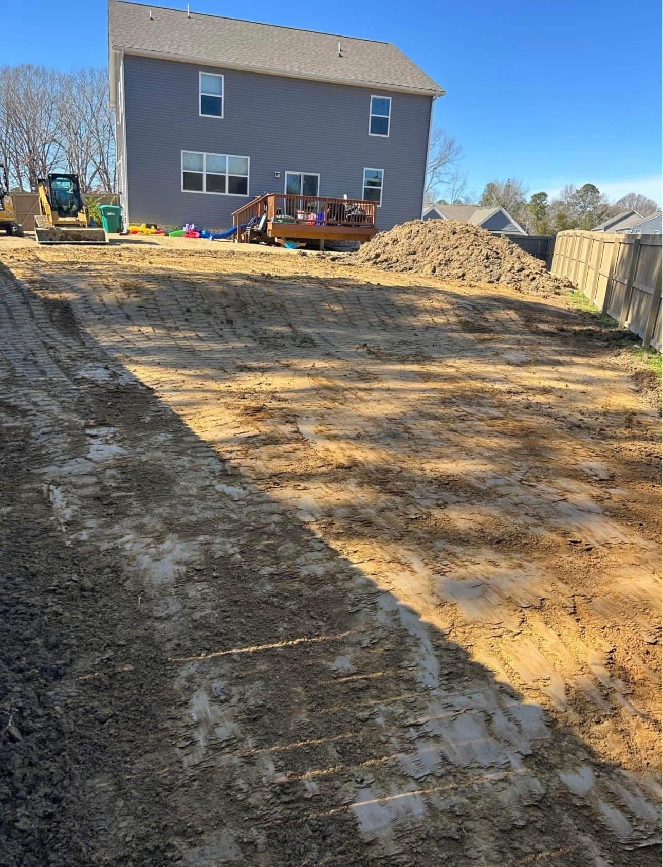 Home construction site with freshly graded yard and a gray house in the background.