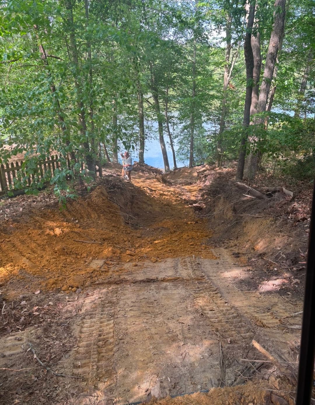 Excavated pathway leading to a lake, surrounded by trees and natural scenery.