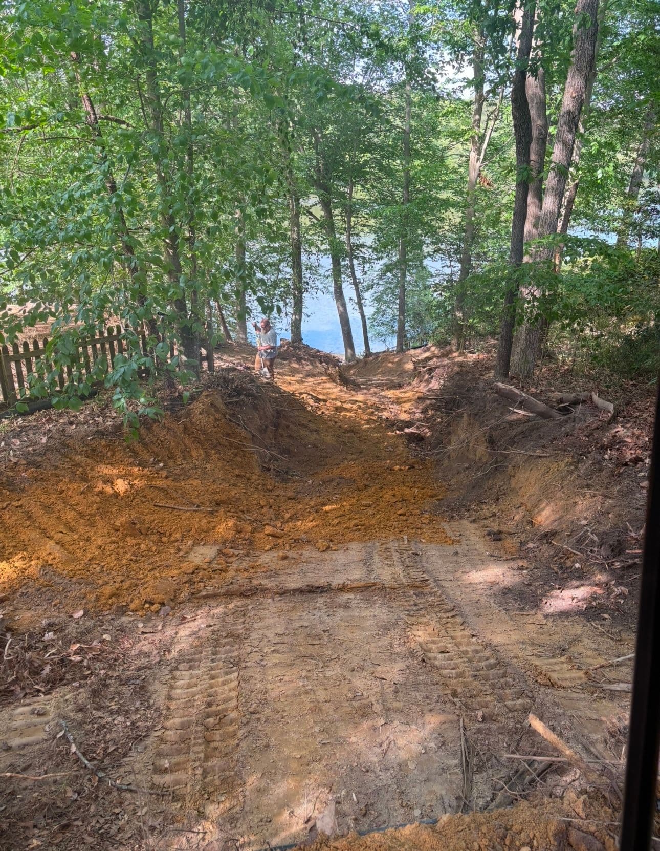 Excavated pathway leading to a lake, surrounded by trees and natural scenery.
