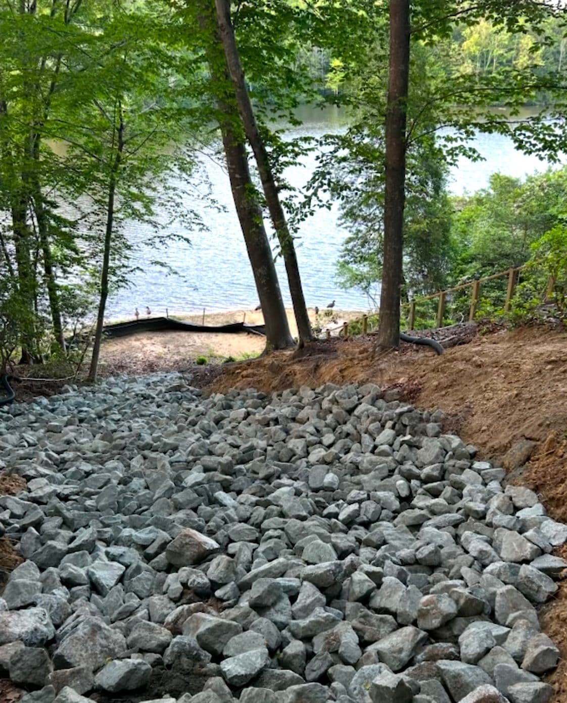 Rocky pathway leads to a serene lake, surrounded by trees and greenery.