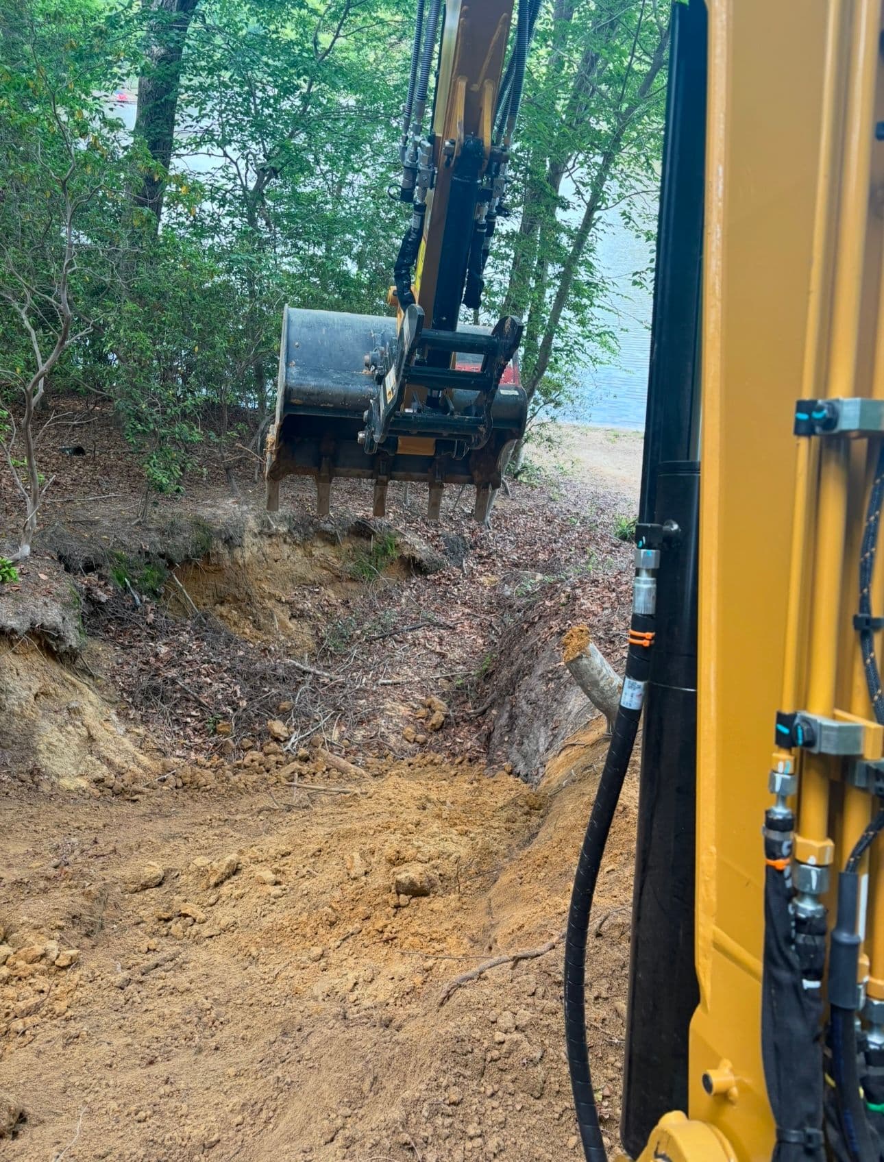 Excavator digging soil near wooded area, showcasing construction and earth-moving equipment.