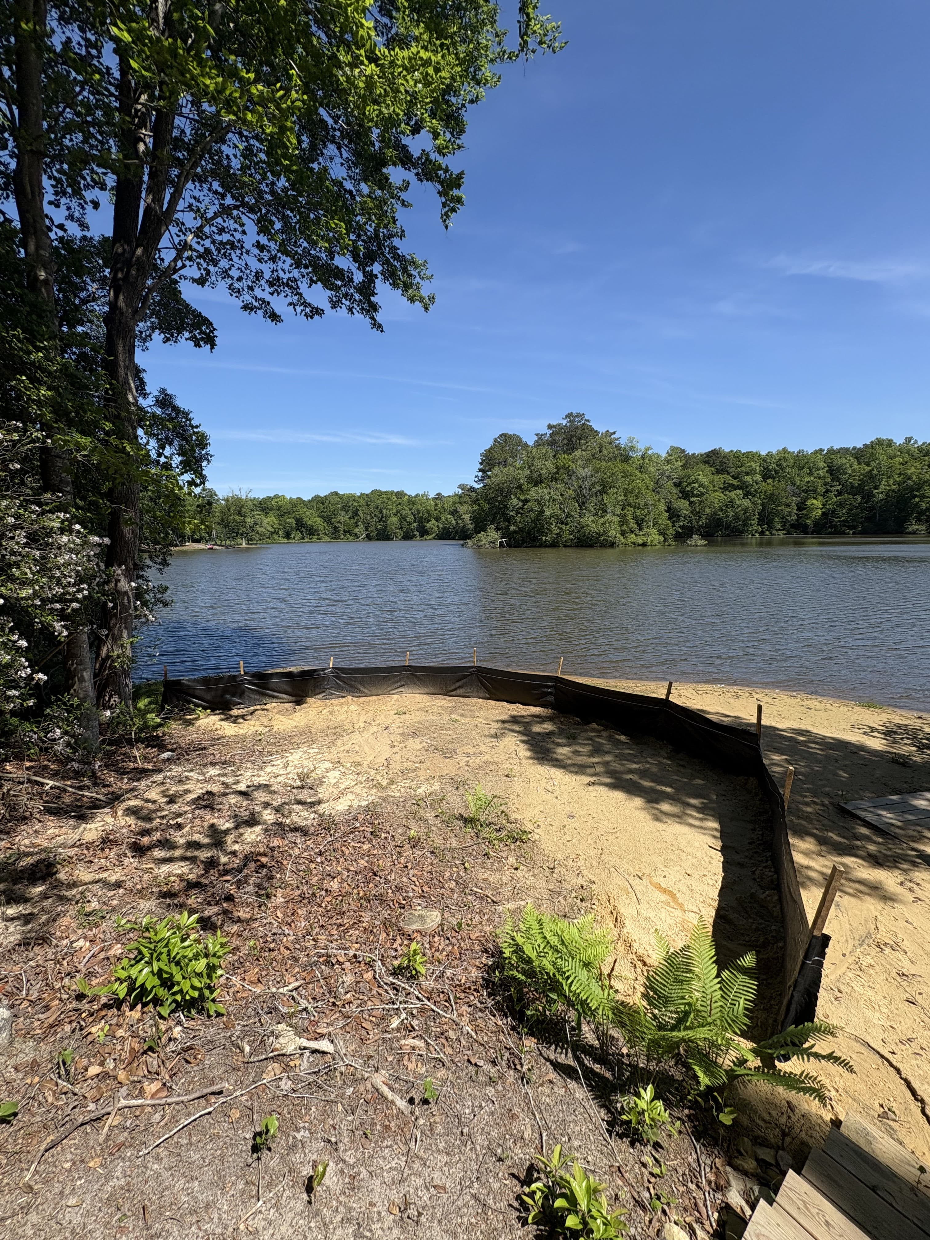 Lake view with sandy shore and erosion control fabric in a lush green landscape.