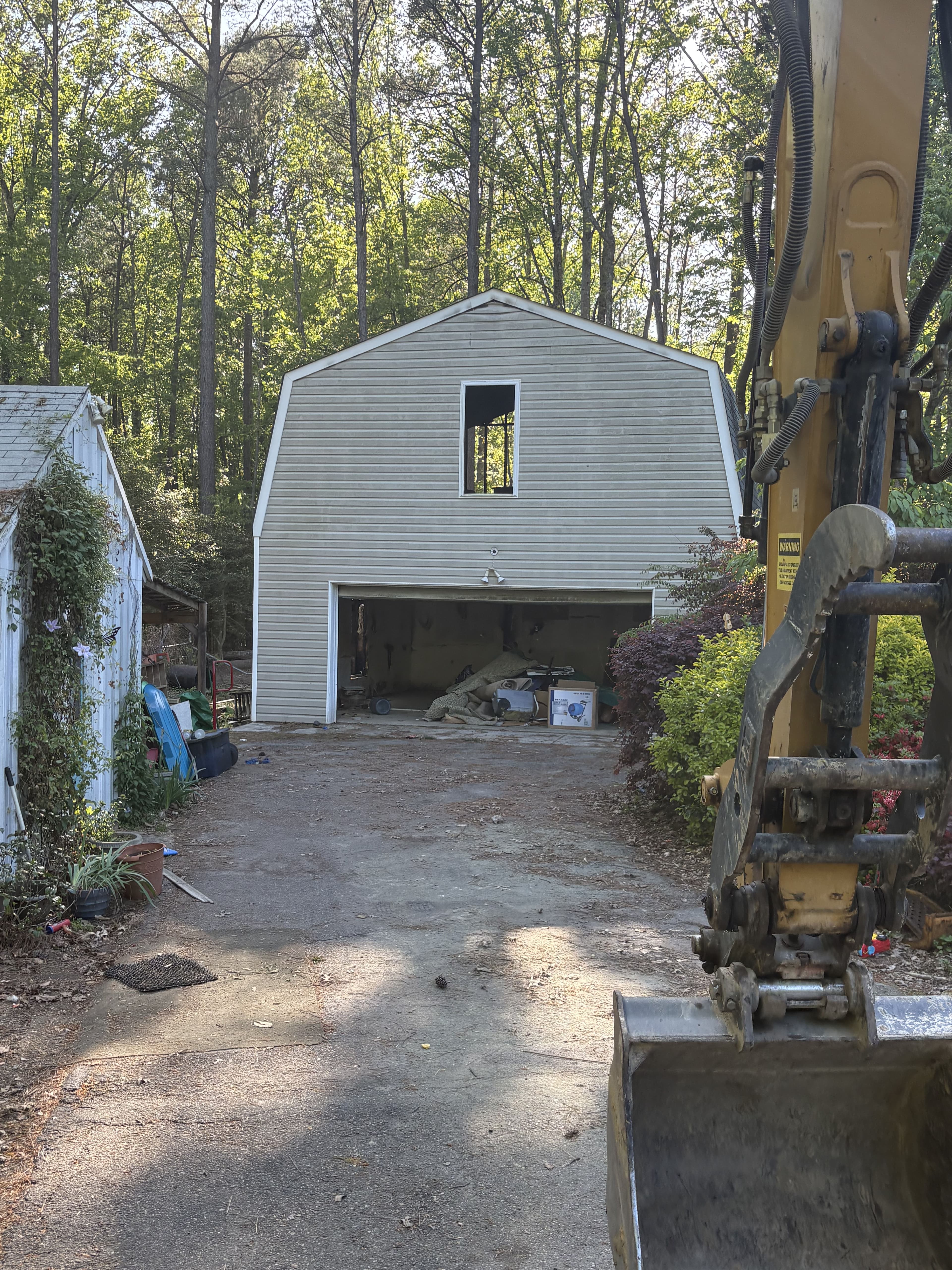Newly built barn-style garage with open window in wooded area, viewed from construction equipment.