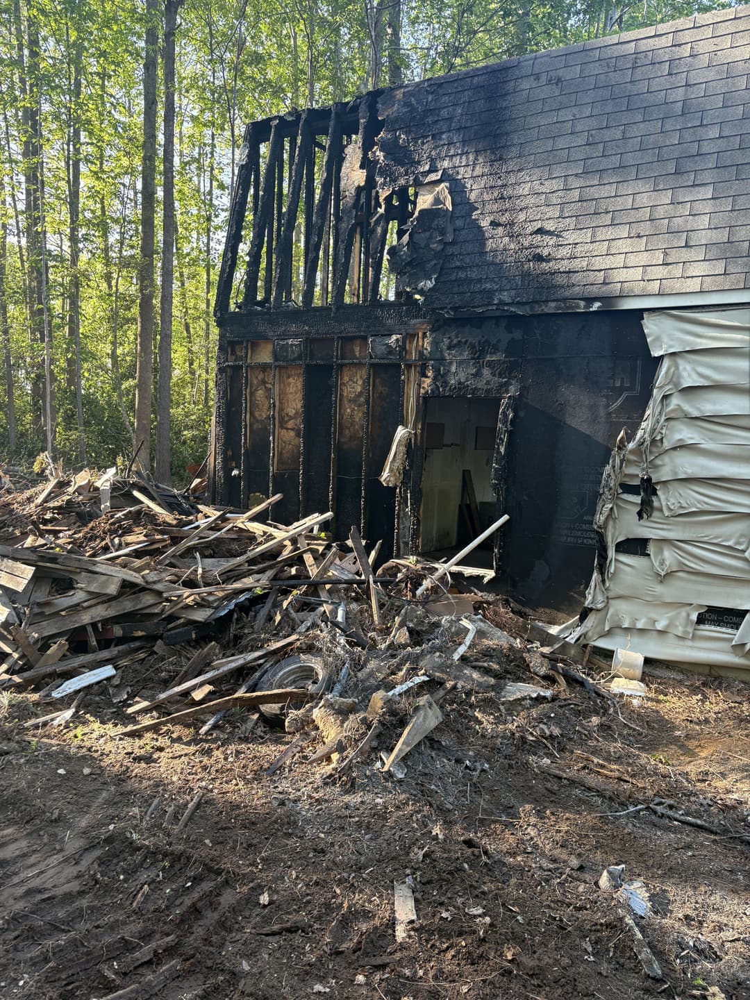 Severely damaged house exterior after fire, surrounded by debris and burnt materials.
