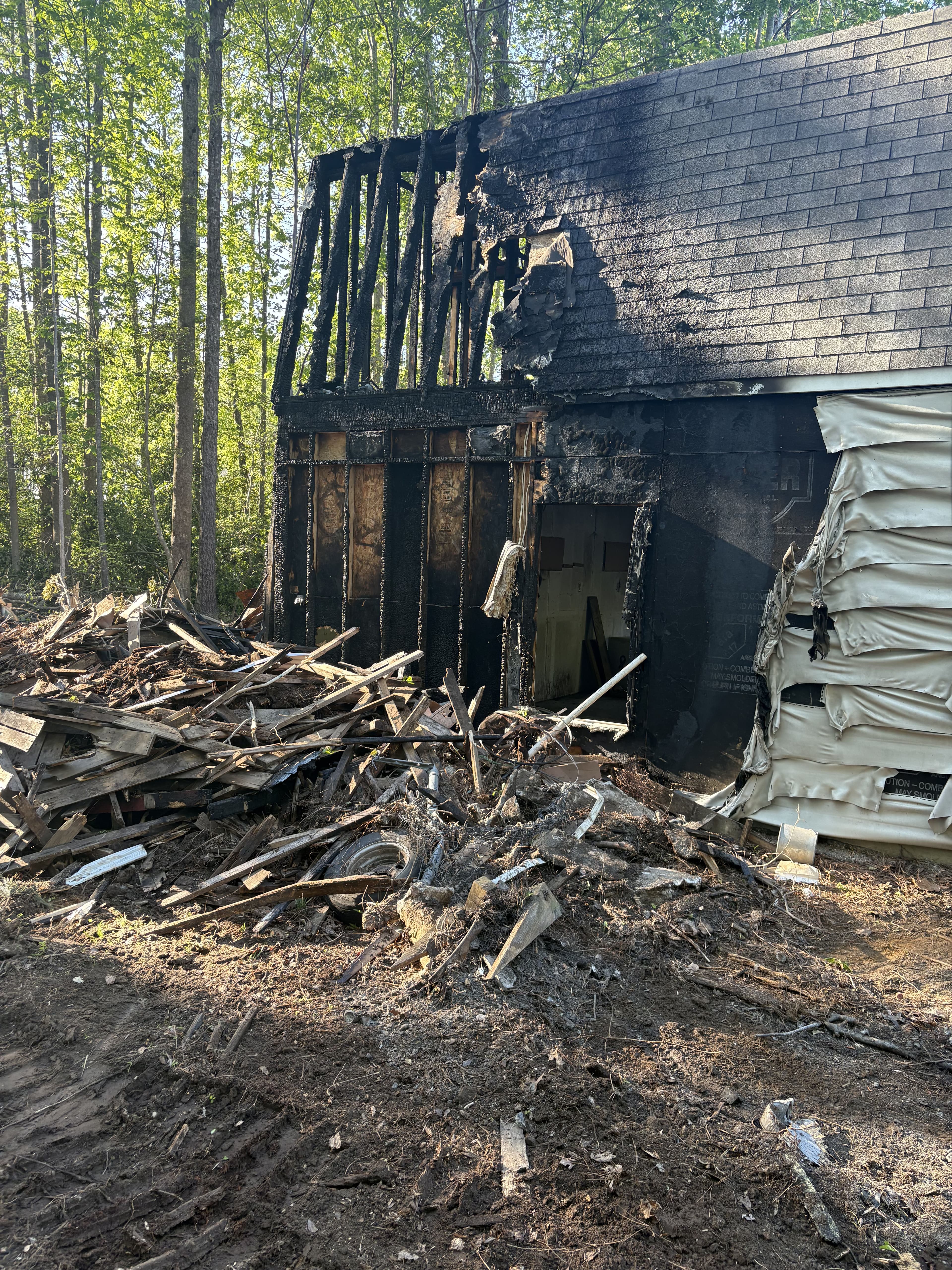 Severely damaged house exterior after fire, surrounded by debris and burnt materials.