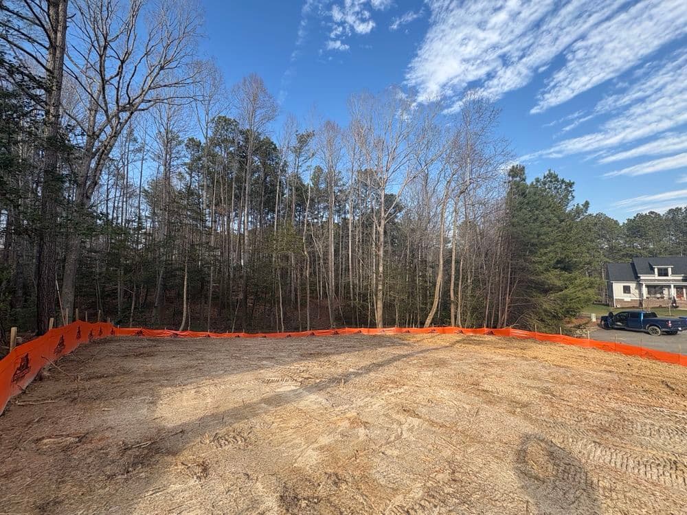 Cleared land with orange safety fence, surrounded by trees, ready for construction.