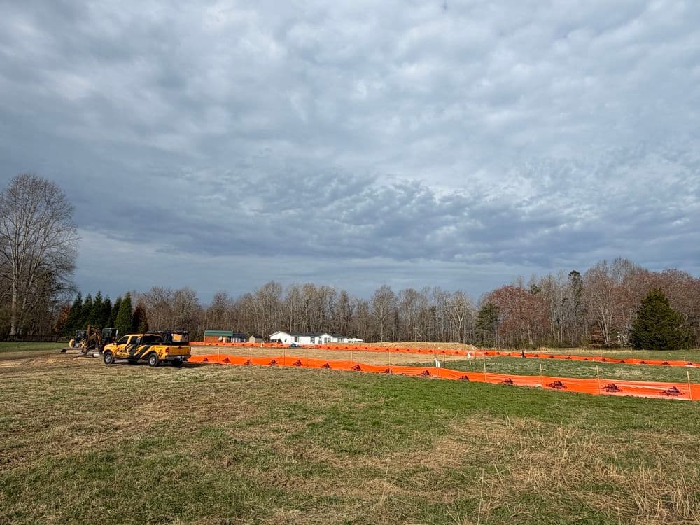Construction site with orange safety fencing and heavy machinery under a cloudy sky.